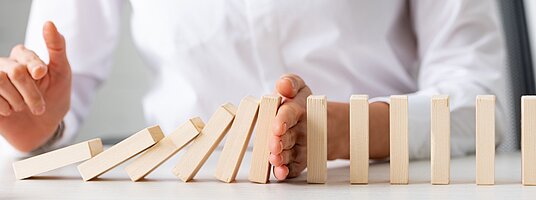 Eine Person stoppt mit der Hand die fallenden hölzernen Dominosteine.